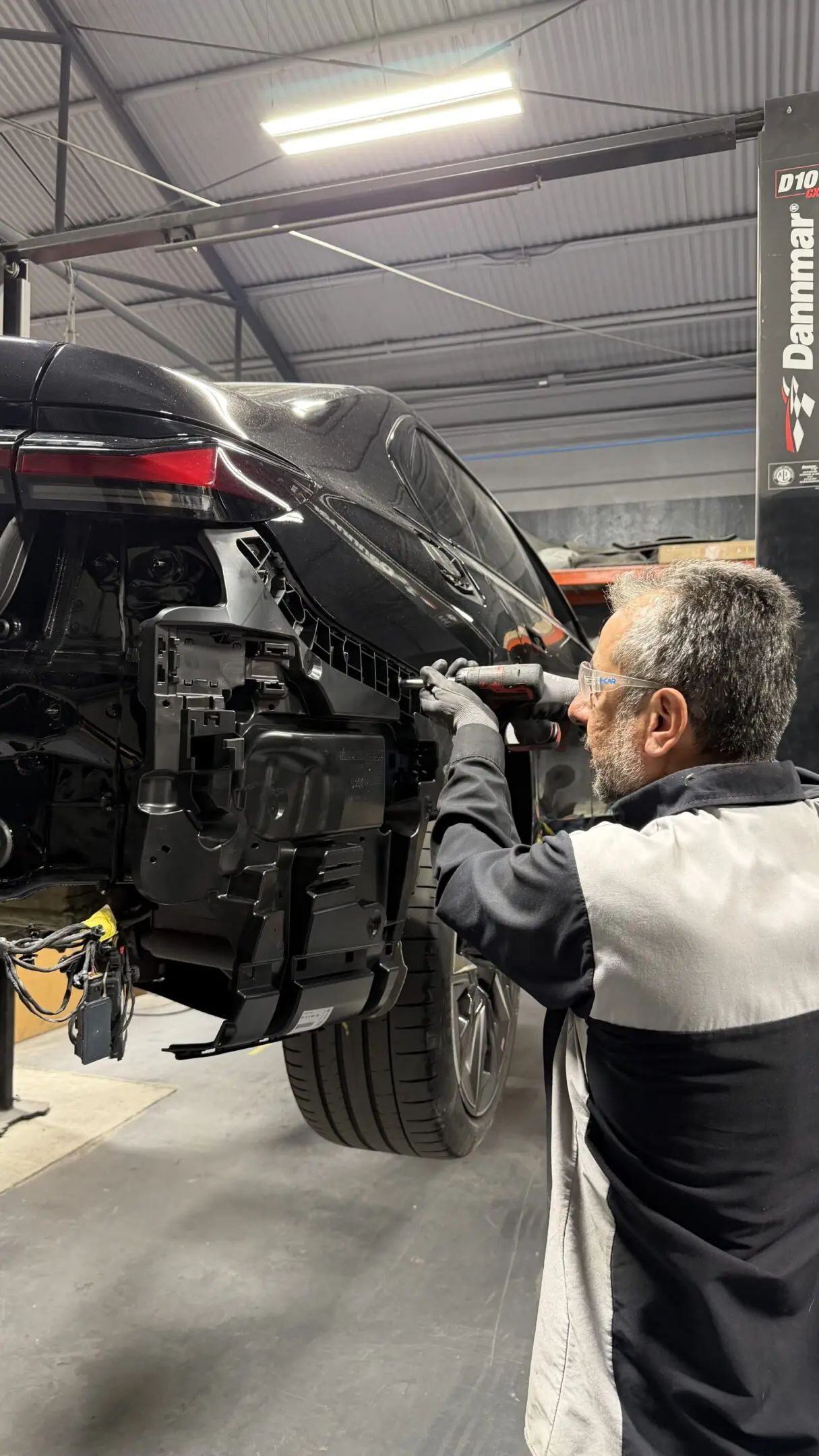 Mechanic working on a car's rear suspension in a garage.